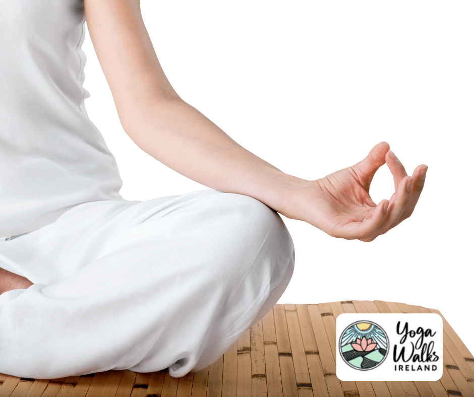 A person in white clothing sits cross-legged on a bamboo mat, hand resting on knee in a meditative pose. The Yoga Walks Ireland logo appears in the bottom right corner.